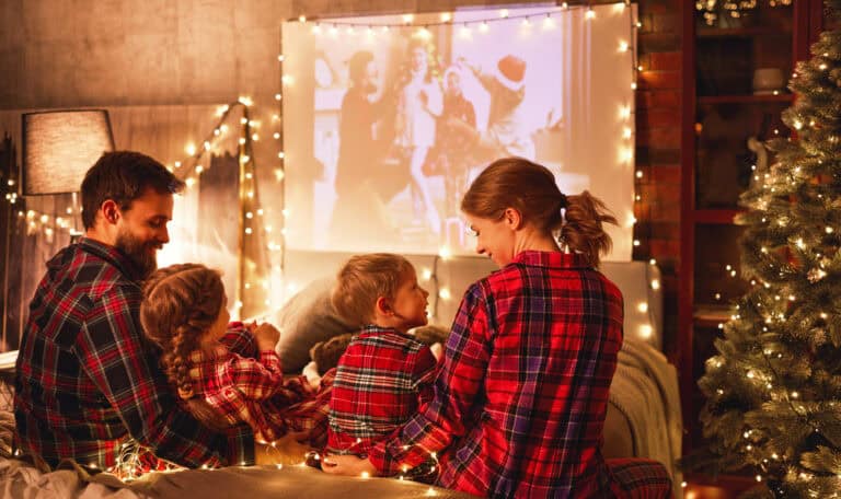 family of four watching Christmas movie on a projector while wearing flannel pajamas