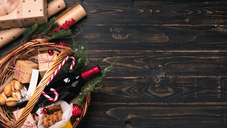 Christmas gift basket with wine, presents, cookies on dark hardwood